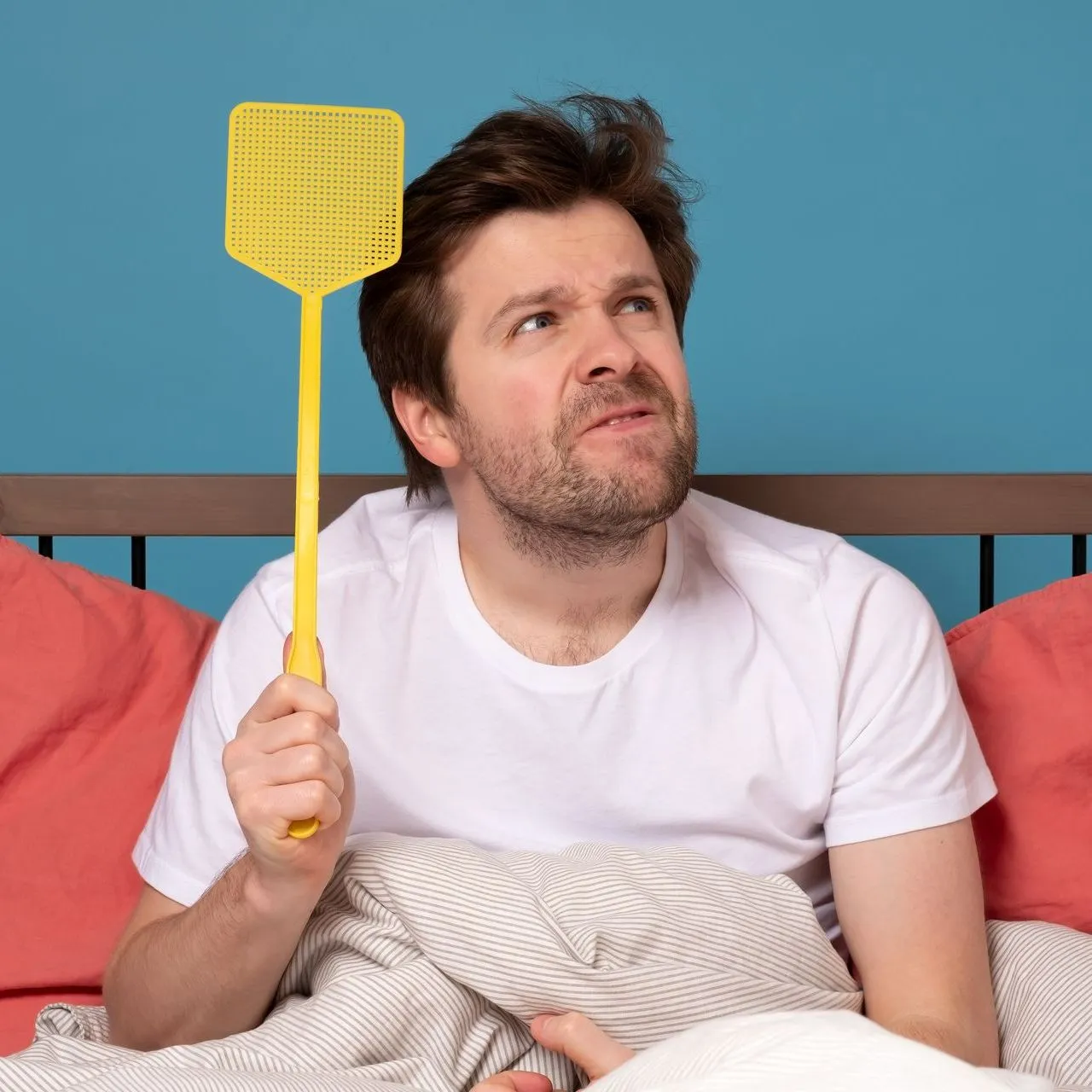 Un homme au lit tient une tapette à la main